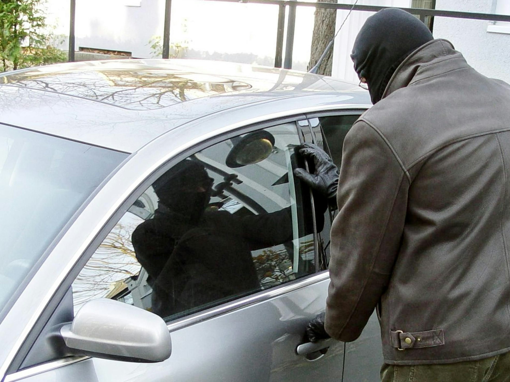 Ein Mann, der sein Gesicht vermummt hat, versucht, ein Auto zu stehlen.