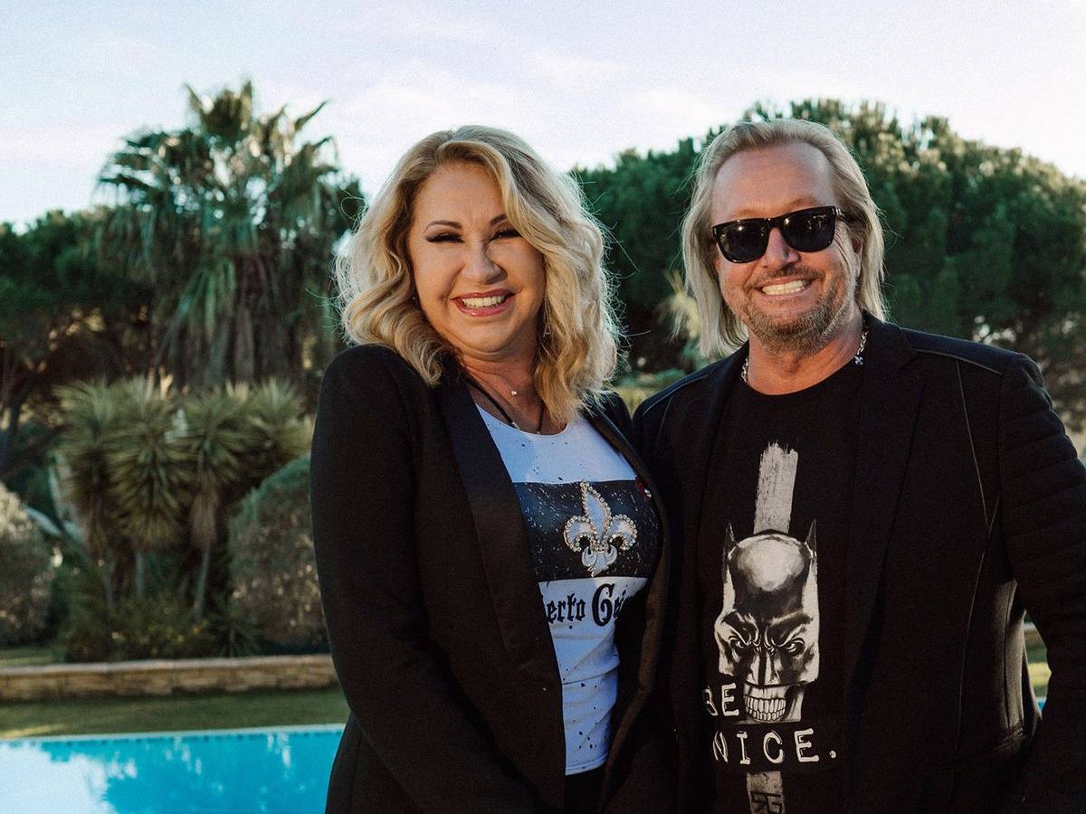 Carmen und Robert Geiss lachen posierend in die Kamera. Im Hintergrund ist die Natur zu sehen.