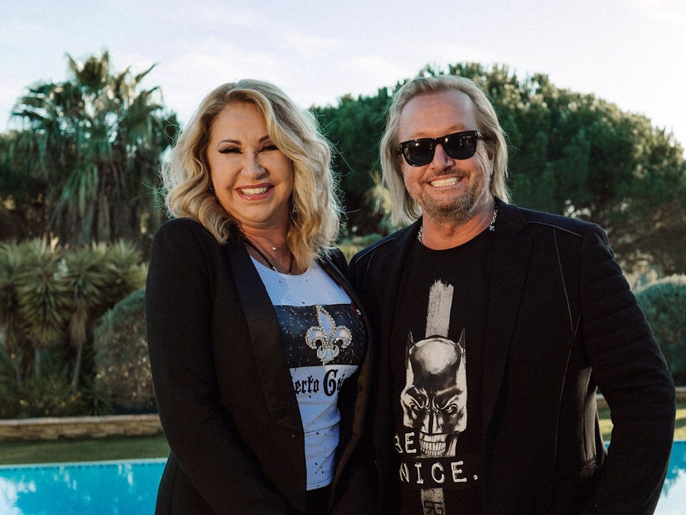 Carmen und Robert Geiss lachen posierend in die Kamera. Im Hintergrund ist die Natur zu sehen.