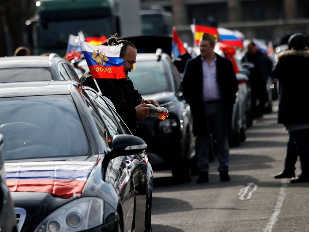 Flaggen mit den russischen Nationalfarben und dem russischen Staatswappen wehen an einem Auto auf dem Olympiaplatz vor dem Olympiastadion. Etwa 900 Menschen haben am Sonntag in Berlin an einem Autokorso mit russischen Fahnen teilgenommen.