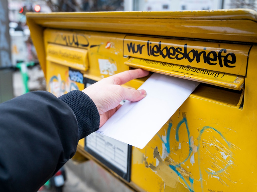 Eine Person wirft einen Brief in einen Briefkasten.