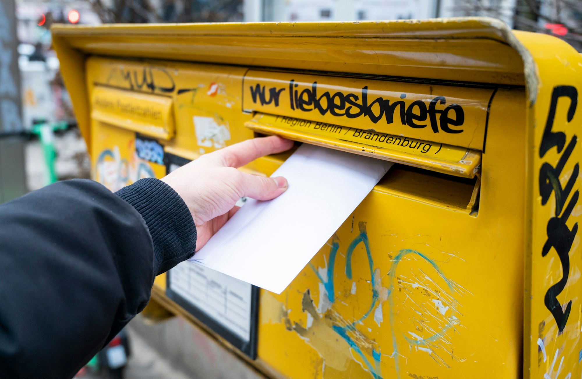 Eine Person wirft einen Brief in einen Briefkasten.
