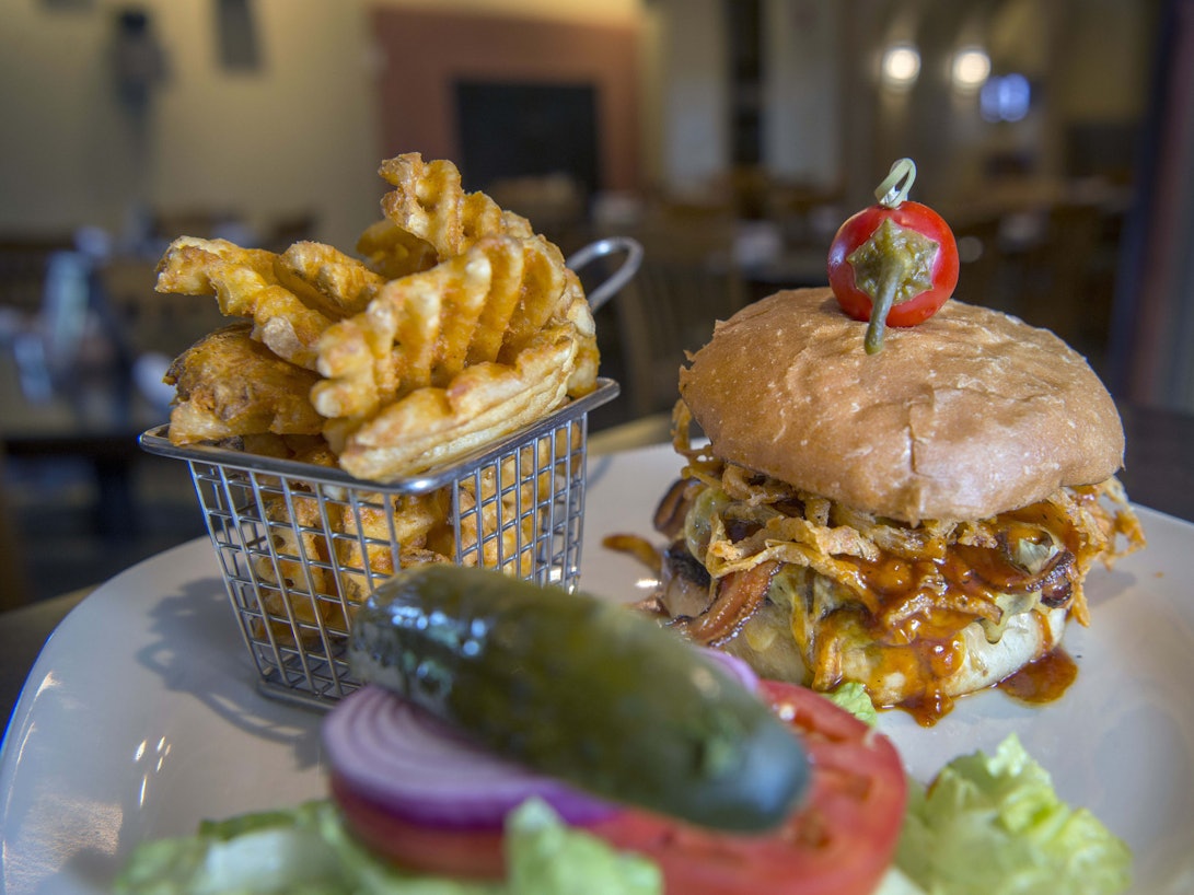 Ein Barbecue-Burger mit Speck und gerösteten Zwiebeln steht neben Gitter-Pommes auf dem Tisch.