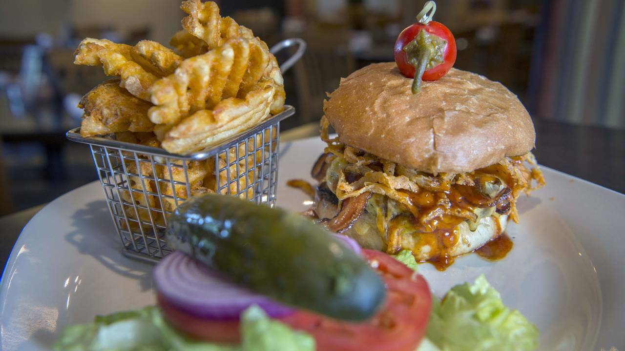 Ein Barbecue-Burger mit Speck und gerösteten Zwiebeln steht neben Gitter-Pommes auf dem Tisch.