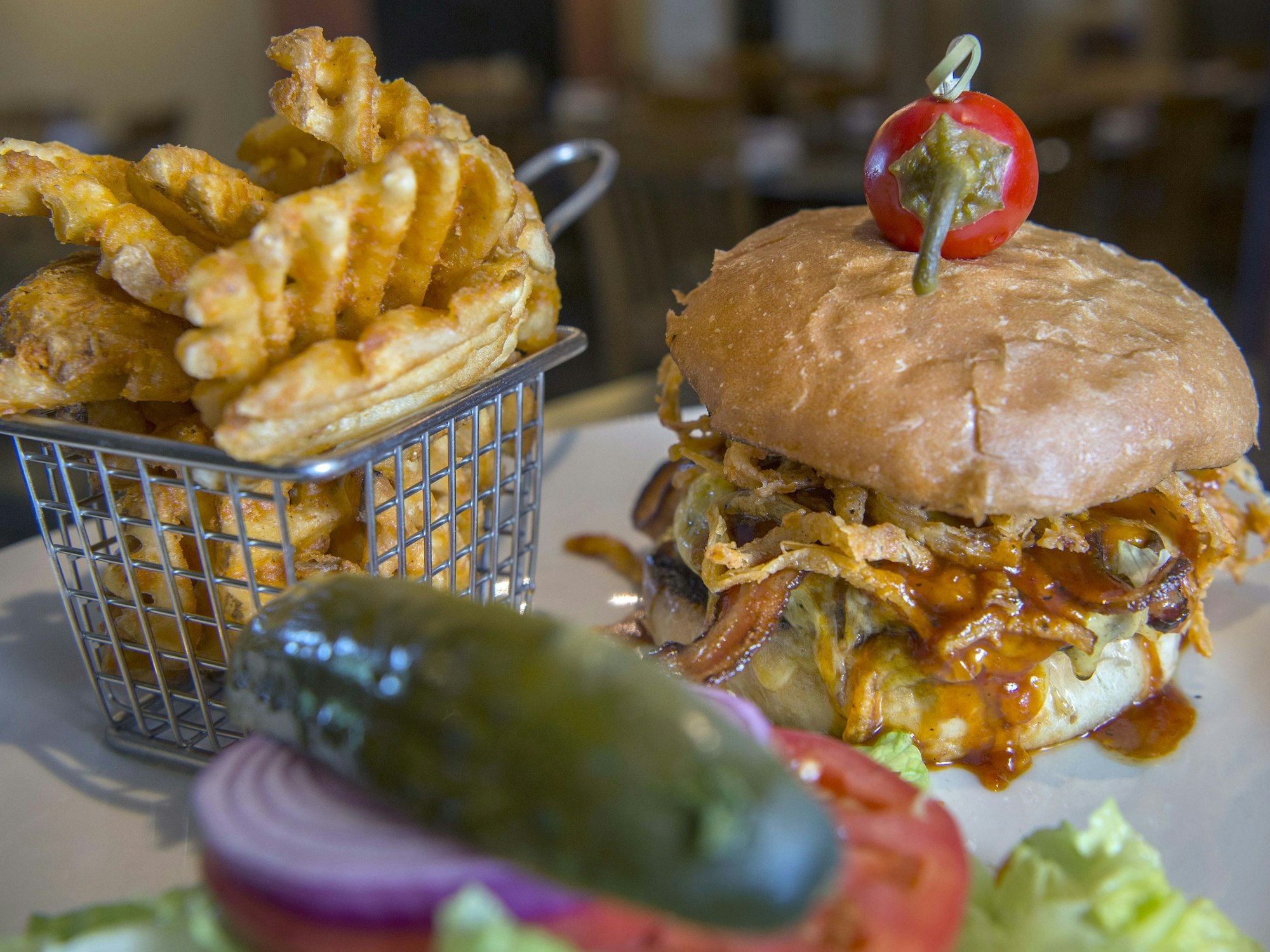 Ein Barbecue-Burger mit Speck und gerösteten Zwiebeln steht neben Gitter-Pommes auf dem Tisch.
