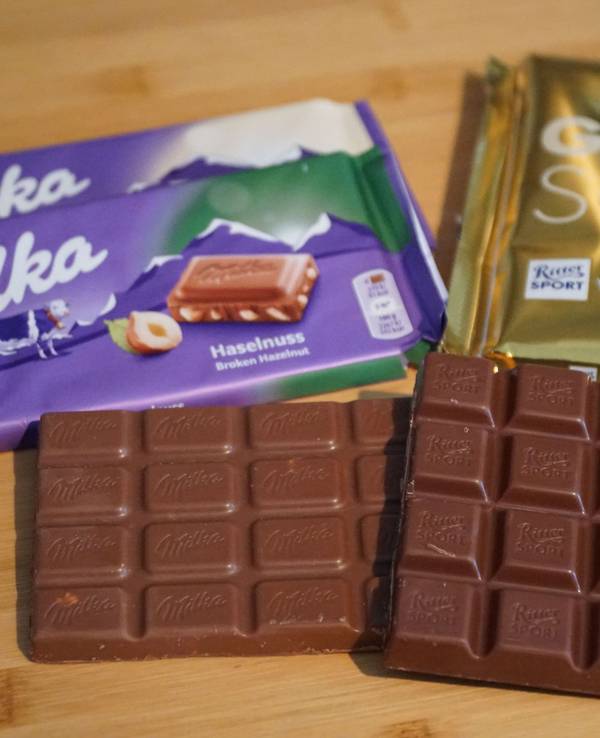 Schokoladentafeln der Marken Ritter Sport und Milka liegen neben einem Maßstab auf einem Tisch.