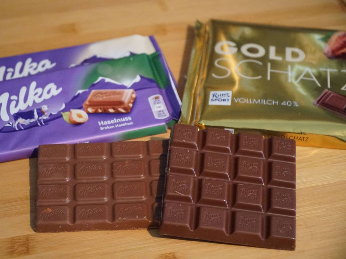 Schokoladentafeln der Marken Ritter Sport und Milka liegen neben einem Maßstab auf einem Tisch.