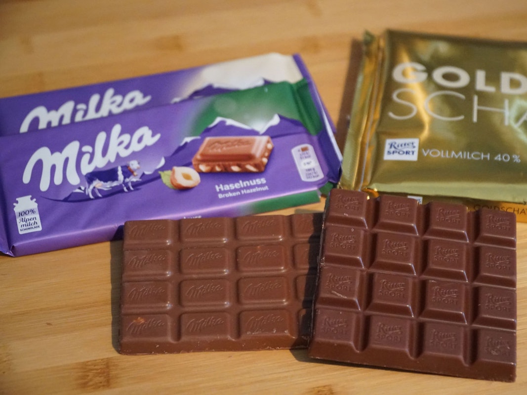Schokoladentafeln der Marken Ritter Sport und Milka liegen neben einem Maßstab auf einem Tisch.