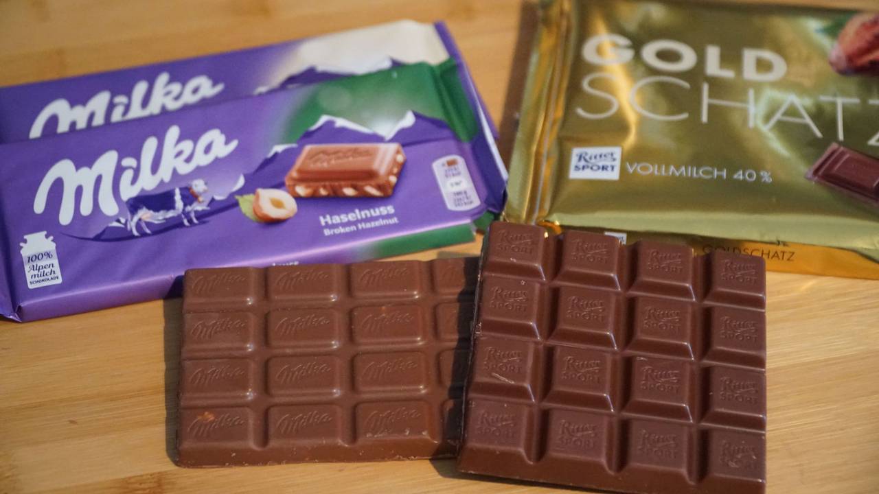 Schokoladentafeln der Marken Ritter Sport und Milka liegen neben einem Maßstab auf einem Tisch.
