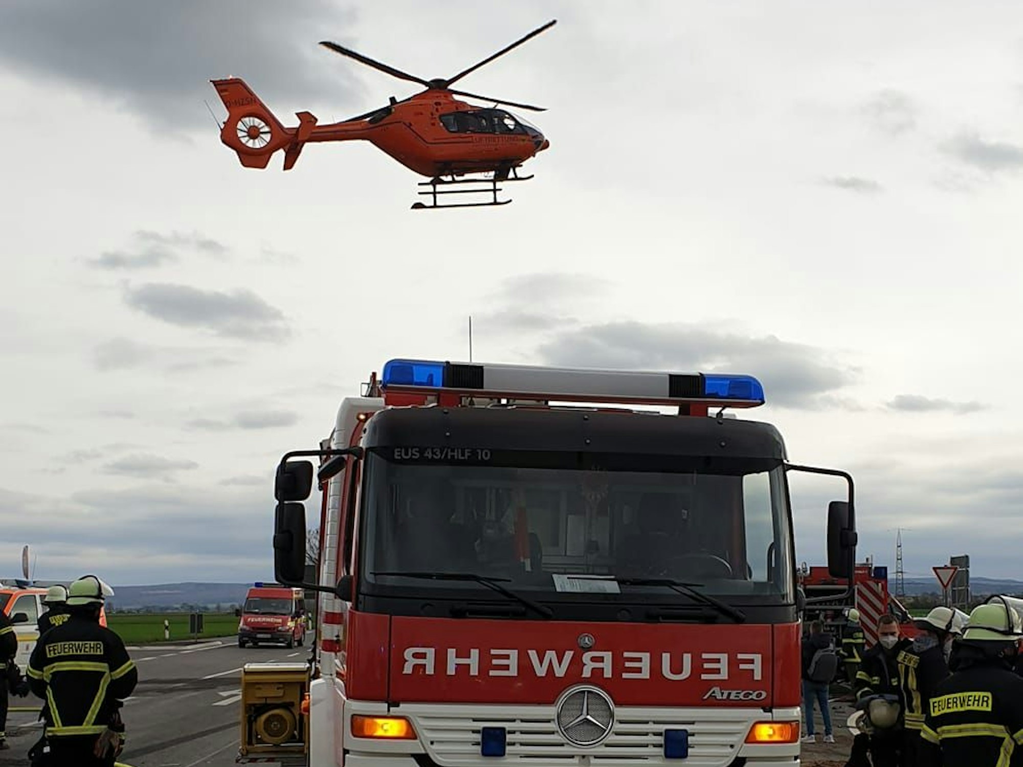 Feuerwehrkräfte sind nach einem Unfall im Einsatz, über ihren Köpfen schwebt ein Rettungshubschrauber.