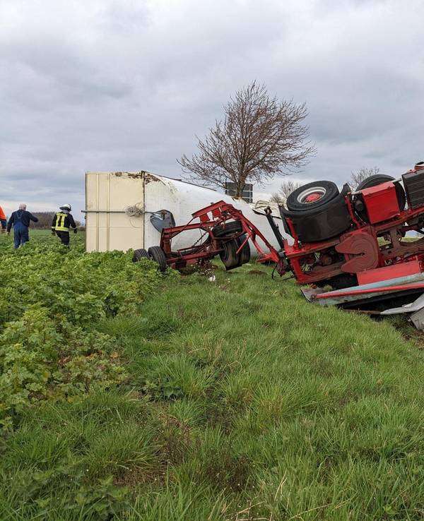 Ein Sattelzug liegt samt Anhänger in einem Feld neben der Straße.