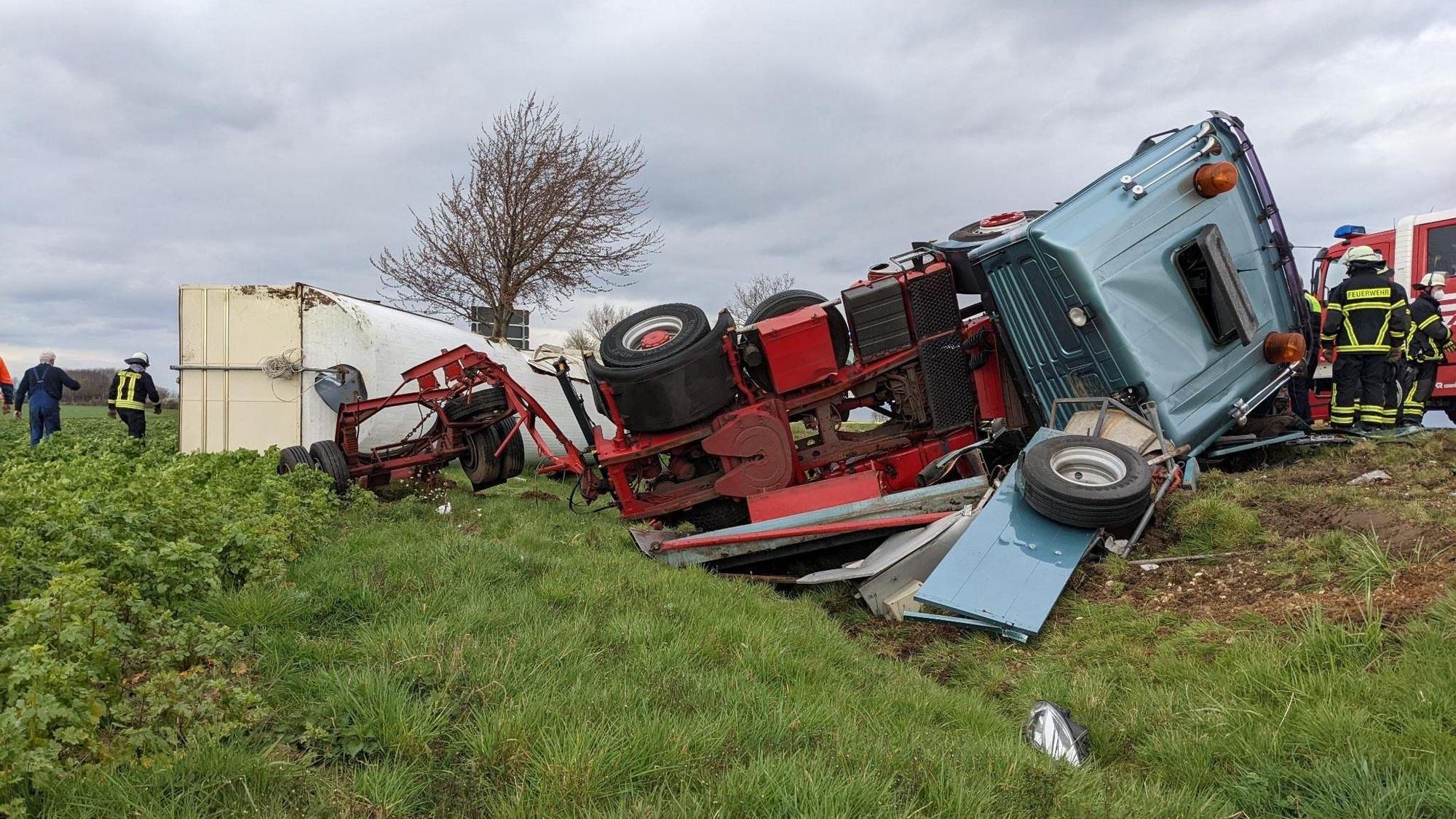 Ein Sattelzug liegt samt Anhänger in einem Feld neben der Straße.