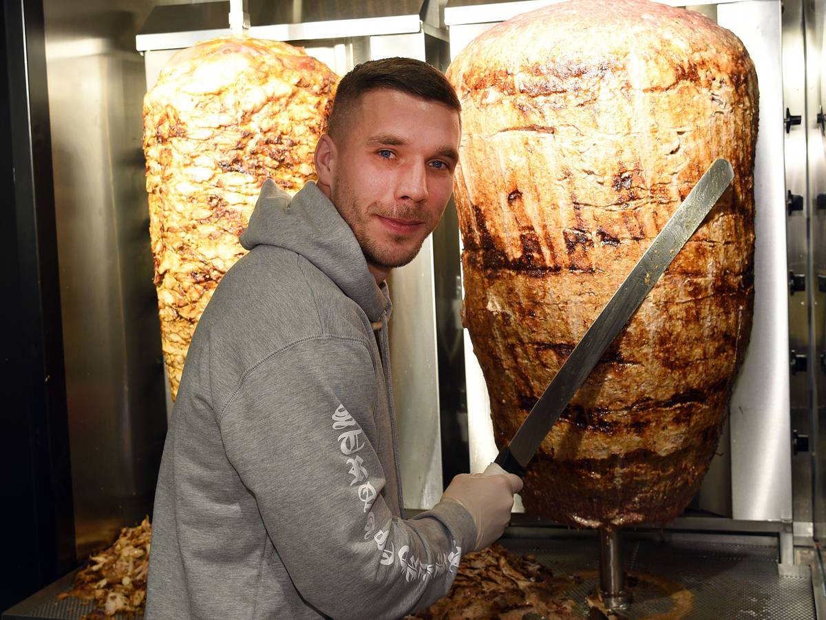 Fußball-Weltmeister Lukas Podolski steht am 06.01.2018 in Köln (Nordrhein-Westfalen) bei der Eröffnung eines Döner-Ladens an einem Dönerspieß.