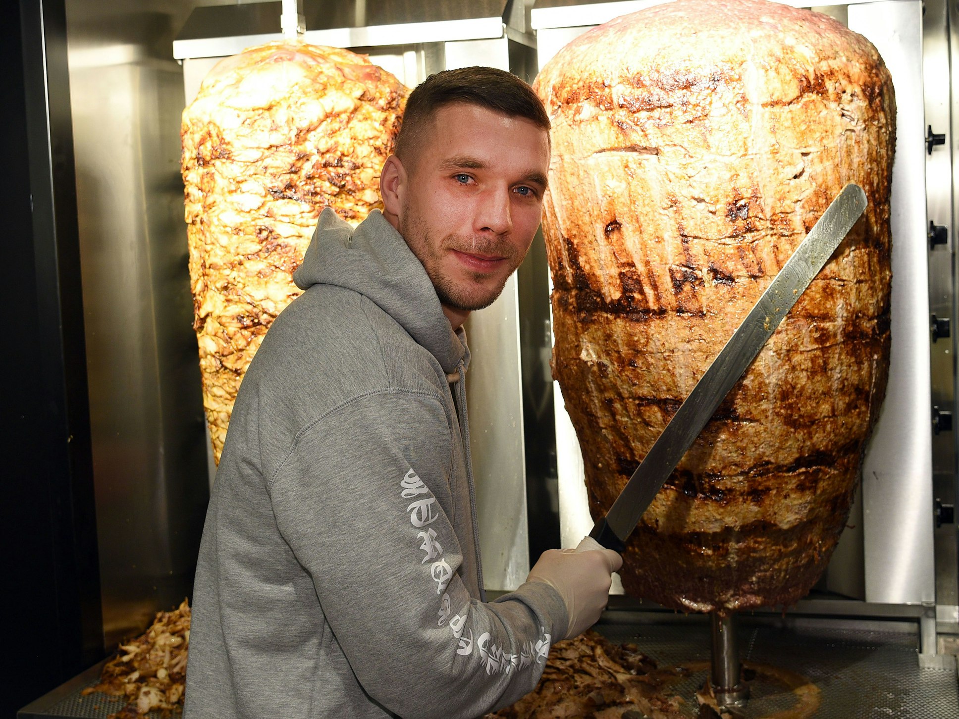Fußball-Weltmeister Lukas Podolski steht am 06.01.2018 in Köln (Nordrhein-Westfalen) bei der Eröffnung eines Döner-Ladens an einem Dönerspieß.
