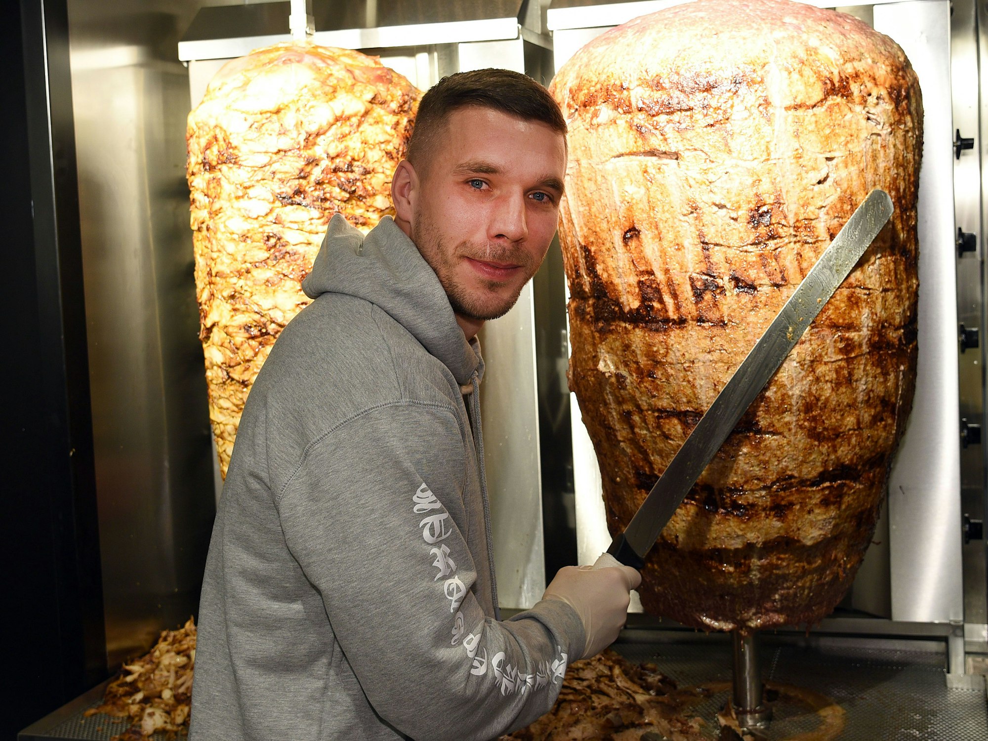 Fußball-Weltmeister Lukas Podolski steht am 06.01.2018 in Köln (Nordrhein-Westfalen) bei der Eröffnung eines Döner-Ladens an einem Dönerspieß.