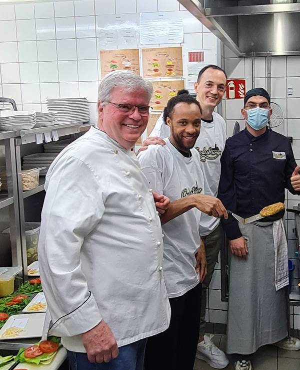 In der Küche des Bonner Restaurants Godesburger stehn Restaurantleiter Bruno Straub, Telekom Baskets-Kapitän Karsten Tadda, Spieler Parker Jackson-Cartwright und Godesburger-Mitarbeiter Zeredesit Omar