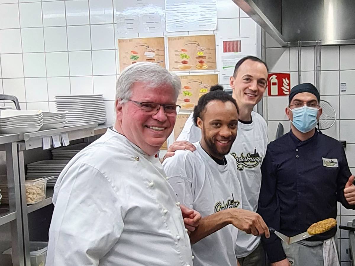In der Küche des Bonner Restaurants Godesburger stehn Restaurantleiter Bruno Straub, Telekom Baskets-Kapitän Karsten Tadda, Spieler Parker Jackson-Cartwright und Godesburger-Mitarbeiter Zeredesit Omar