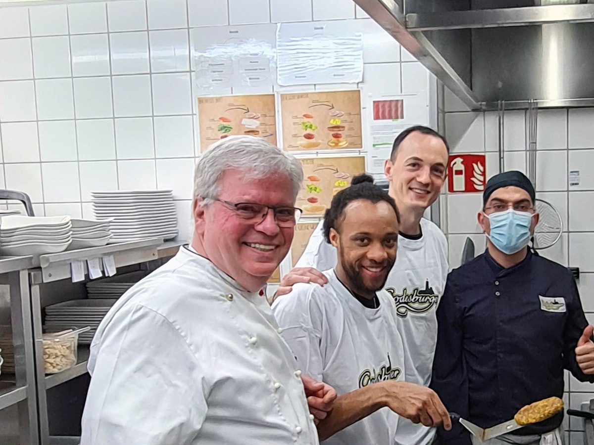 In der Küche des Bonner Restaurants Godesburger stehn Restaurantleiter Bruno Straub, Telekom Baskets-Kapitän Karsten Tadda, Spieler Parker Jackson-Cartwright und Godesburger-Mitarbeiter Zeredesit Omar