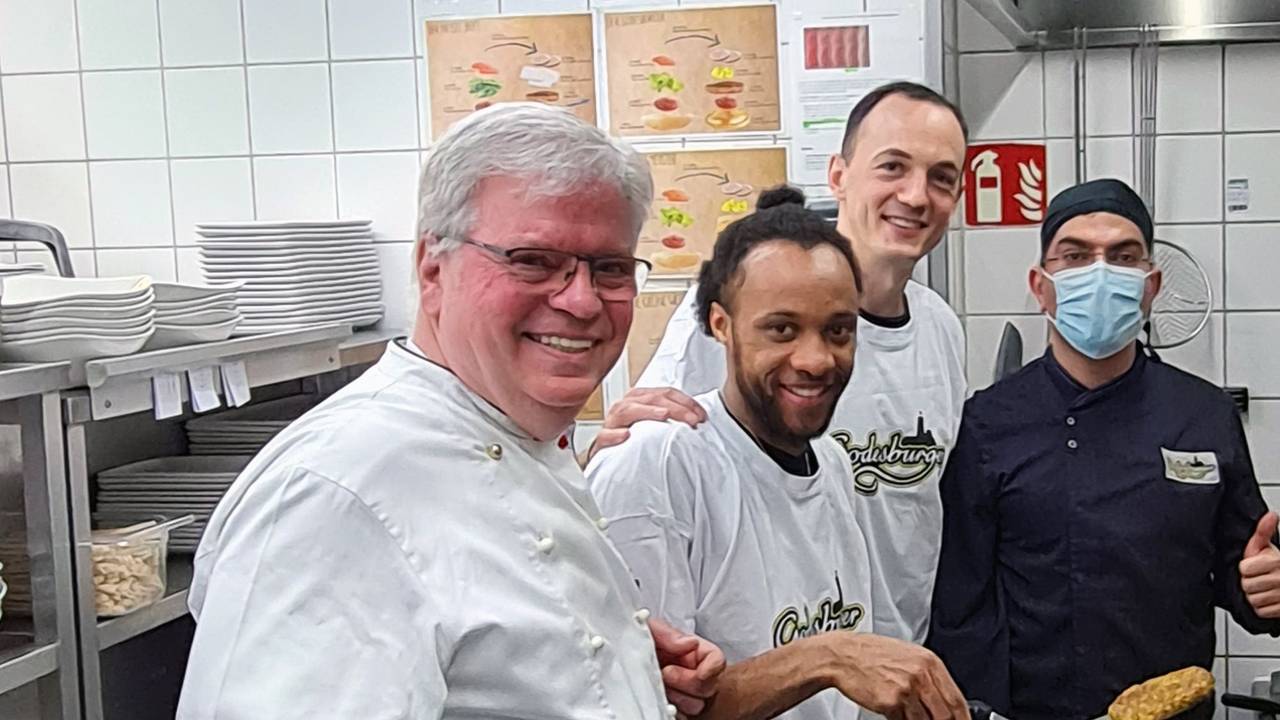 In der Küche des Bonner Restaurants Godesburger stehn Restaurantleiter Bruno Straub, Telekom Baskets-Kapitän Karsten Tadda, Spieler Parker Jackson-Cartwright und Godesburger-Mitarbeiter Zeredesit Omar