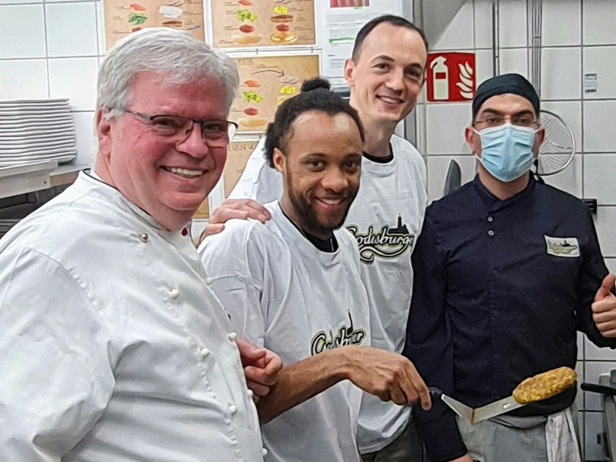 In der Küche des Bonner Restaurants Godesburger stehn Restaurantleiter Bruno Straub, Telekom Baskets-Kapitän Karsten Tadda, Spieler Parker Jackson-Cartwright und Godesburger-Mitarbeiter Zeredesit Omar