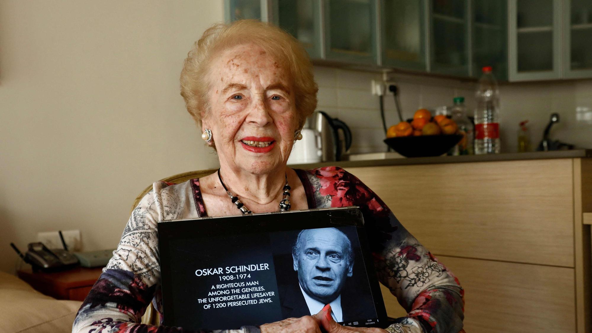 Mimi Reinhardt sitzt auf einem Stuhl, während sie ein Foto von Oskar Schindler in den Händen hält.