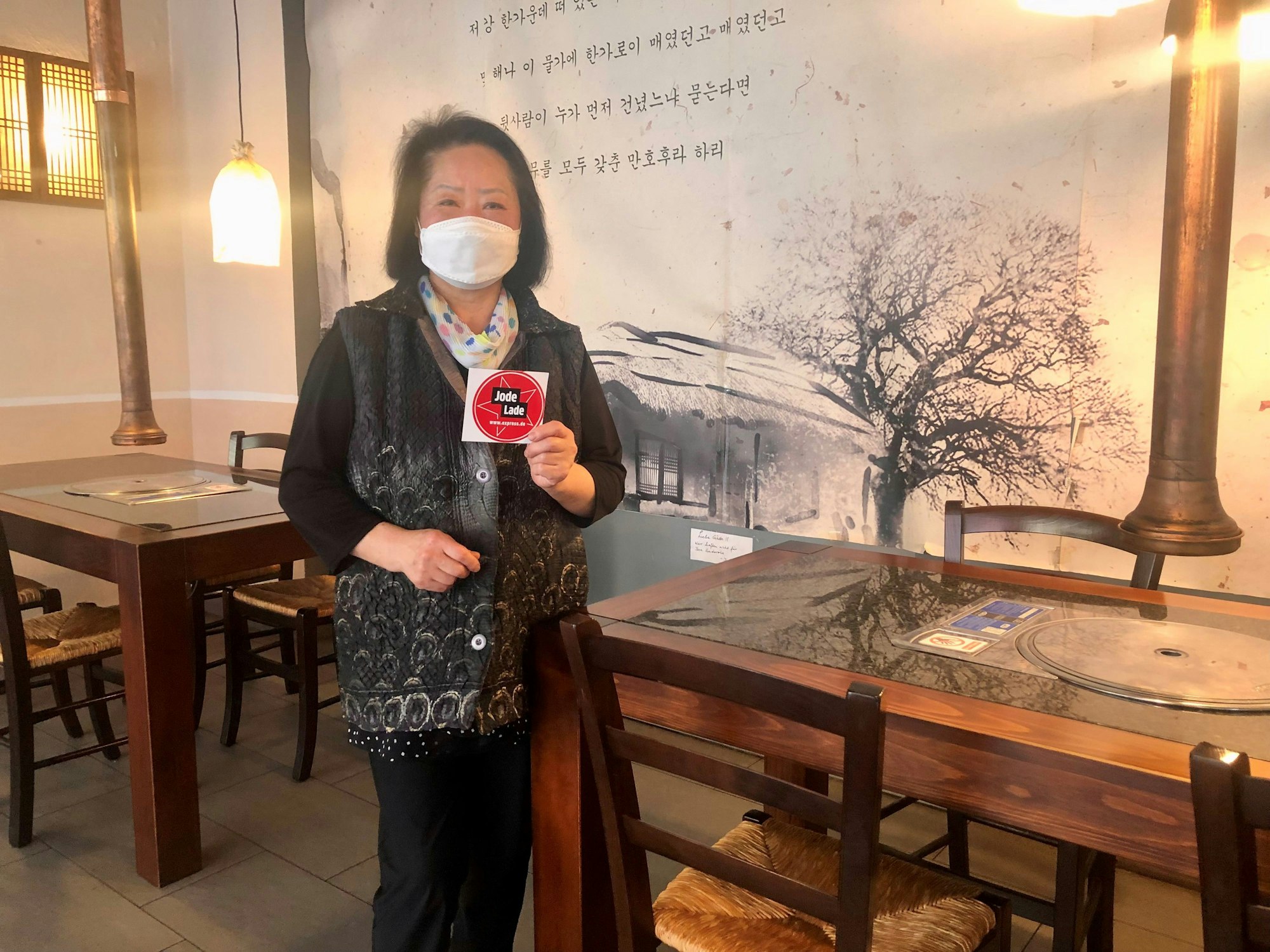 Die Inhaberin des koreanischen Restaurants Nakwon, Joeng Sook Choe Lee, hält das Jode Lade-Gütesiegel in die Kamera.