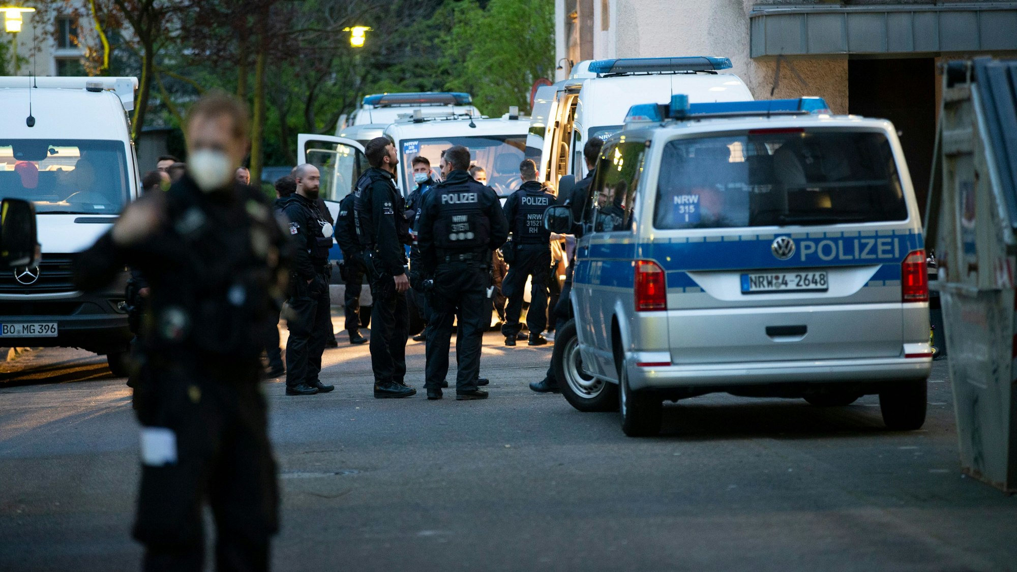 Einsatzkräfte der Polizei sowie Polizeifahrzeuge stehen vor einer Flüchtlingsunterkunft.