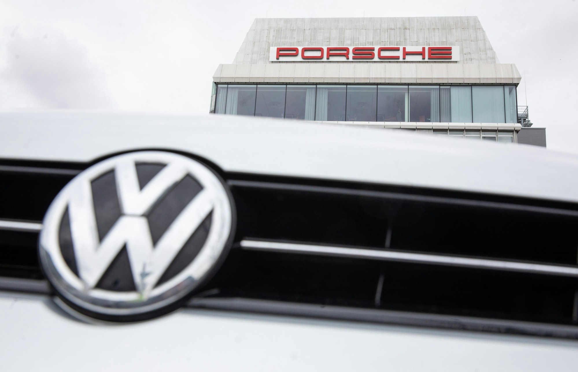 VW-Logo vor Porsche Gebäude.