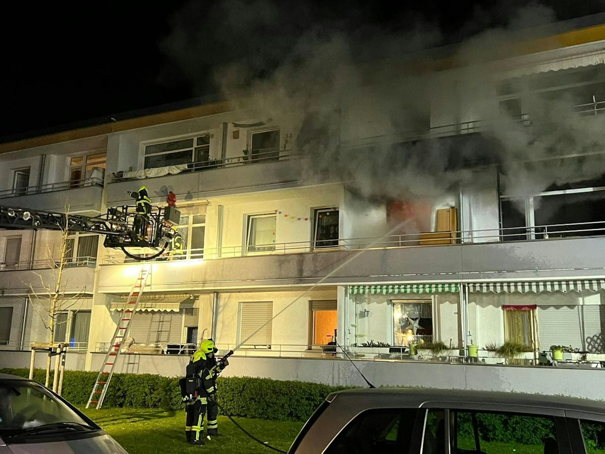 Aus einer Wohnung im ersten Stock eines Mehrfamilienhauses dringt dichter Rauch, ein Feuerwehrmann hält mit dem Schlauch drauf.