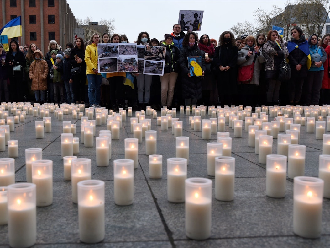 Zahlreiche Kerzen stehen auf einem Platz, der von Menschen gesäumt ist.