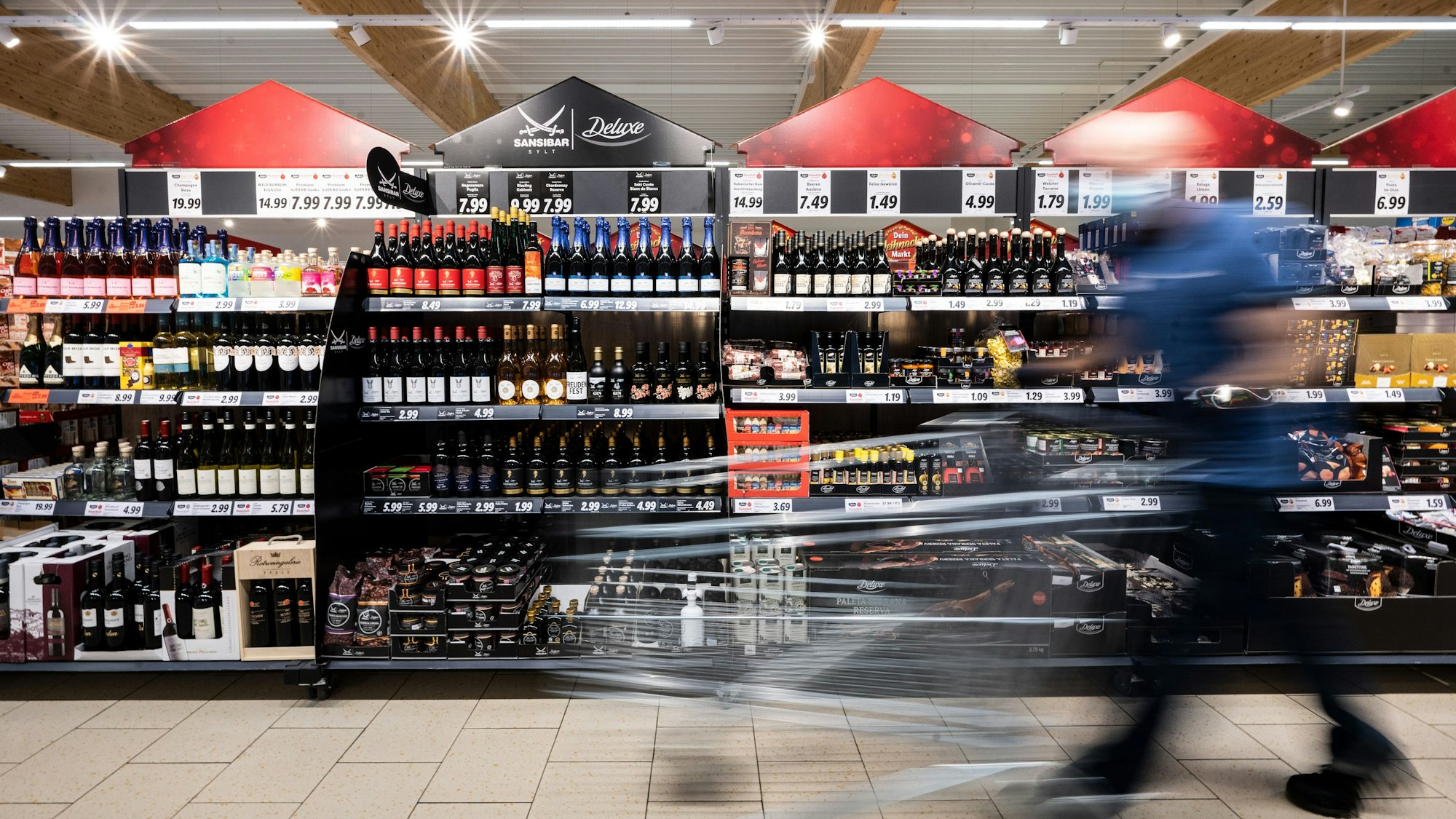 Ein Mann geht mit seinem Einkaufswagen in einer Lidl-Filiale an Regalen mit Sansibar und Deluxe-Produkten vorbei.