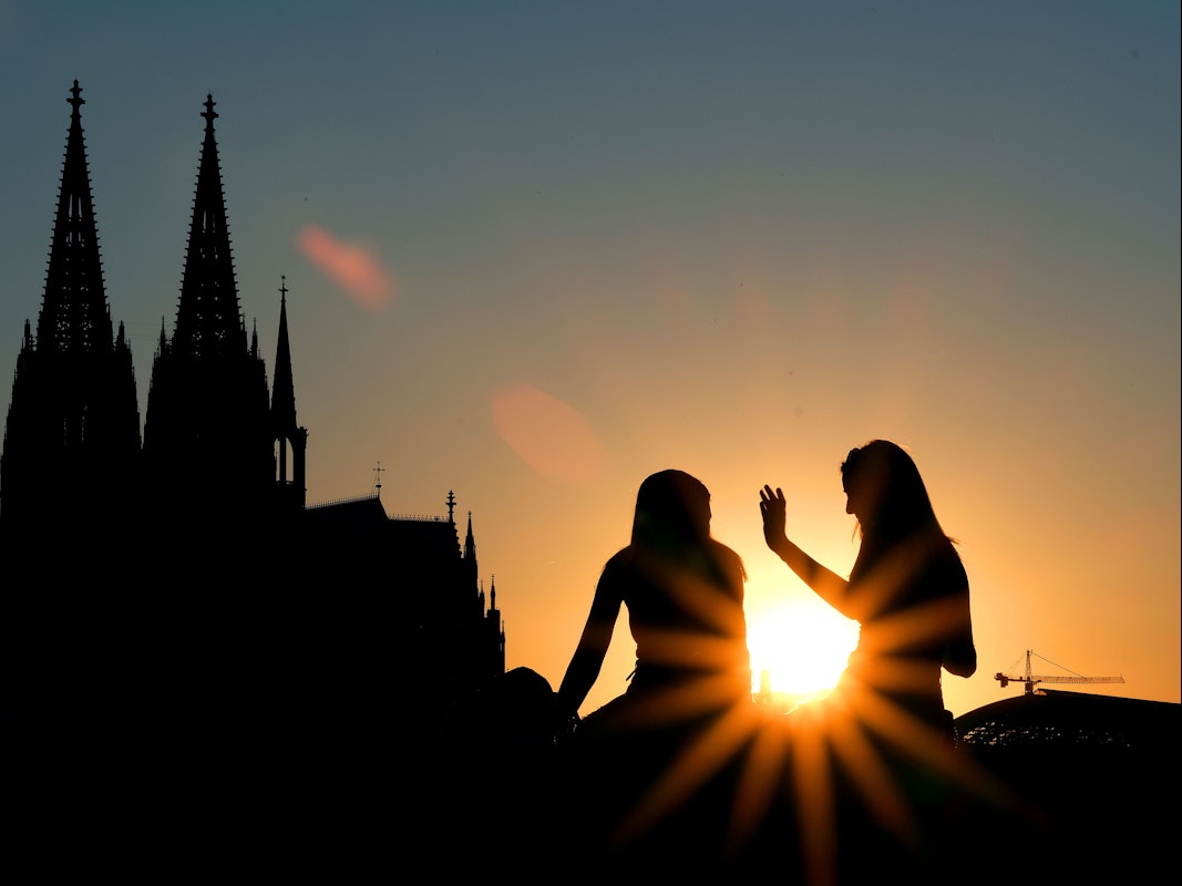 Zwei Frauen sitzen im Sonnenuntergang am Rheinboulevard vor dem Dom.