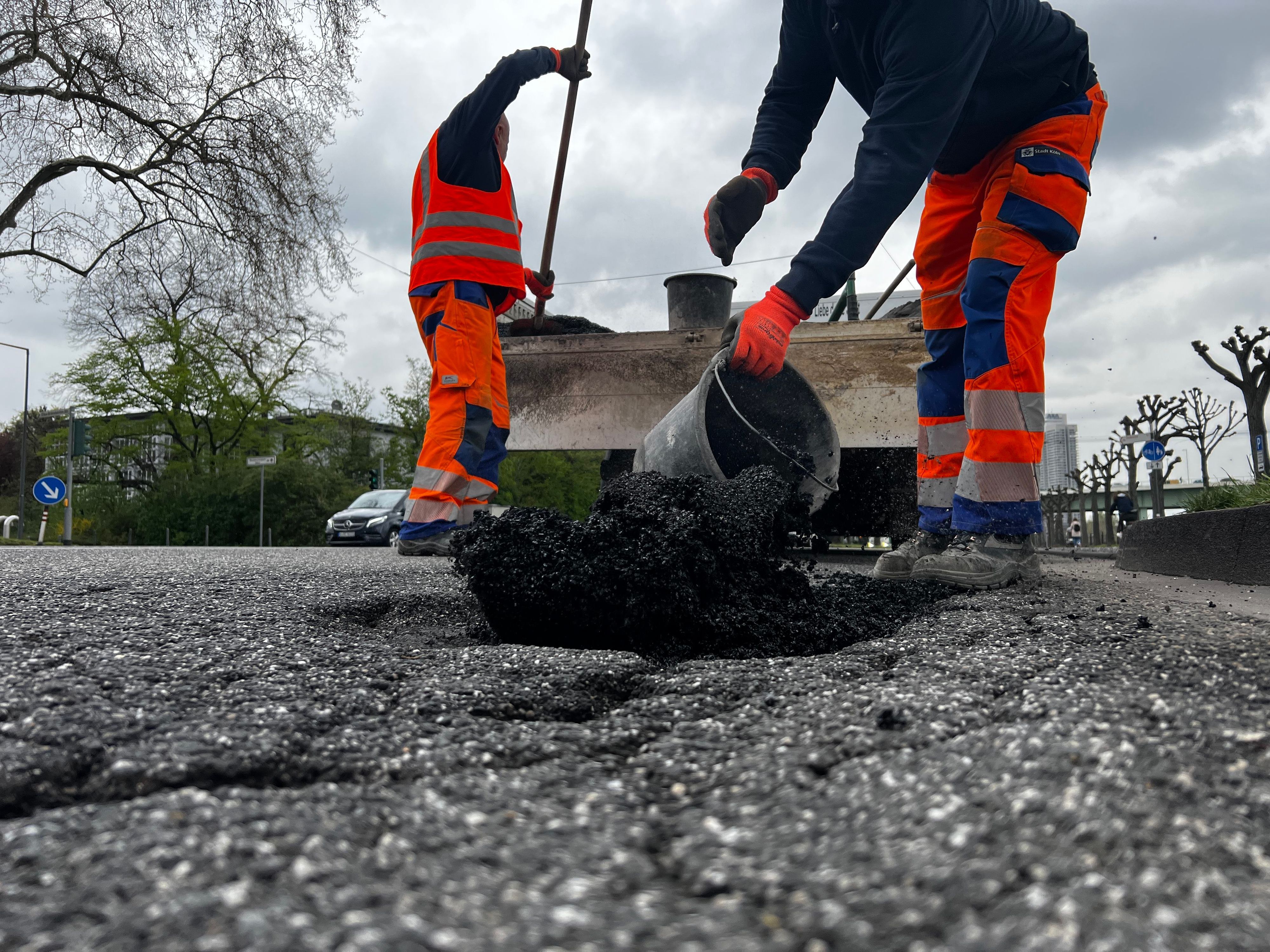 Zwei Bauarbeiter bessern ein Schlagloch in Köln aus.