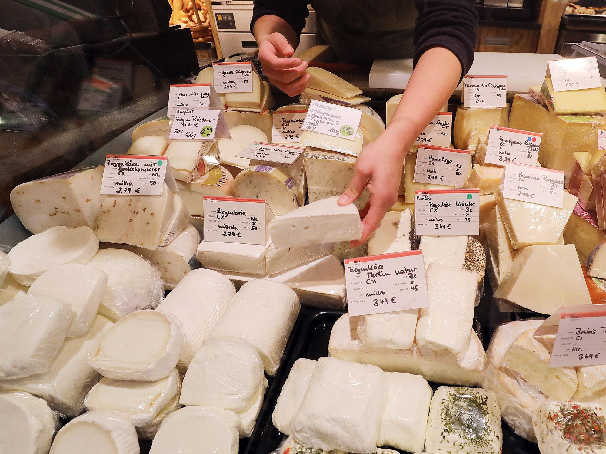 Eine Mitarbeiterin eines Bioladens sortiert an der Käsetheke verschiedene Sorten Ziegenkäse (l)