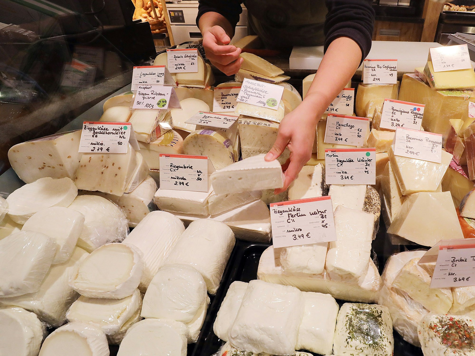 Eine Mitarbeiterin eines Bioladens sortiert an der Käsetheke verschiedene Sorten Ziegenkäse (l)