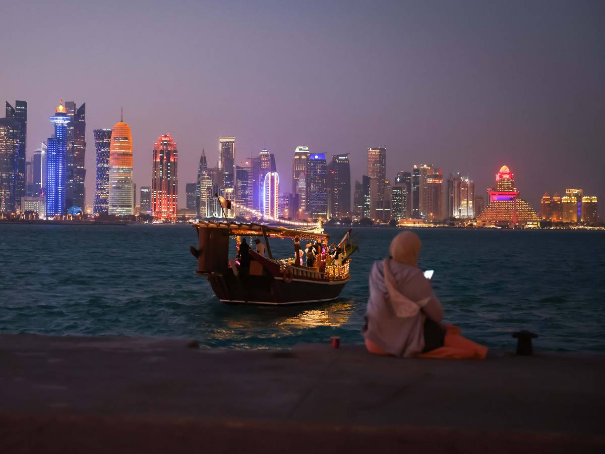 Eine Frau schaut auf ihr Smartphone vor der Skyline von West Bay Doha in Katar