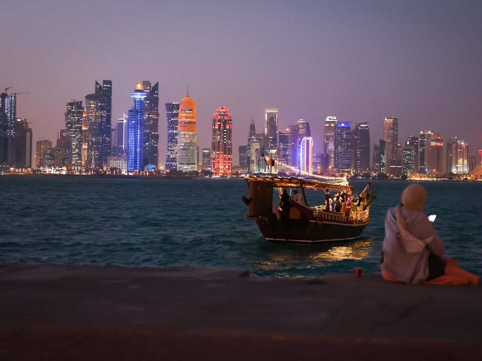 Eine Frau schaut auf ihr Smartphone vor der Skyline von West Bay Doha in Katar