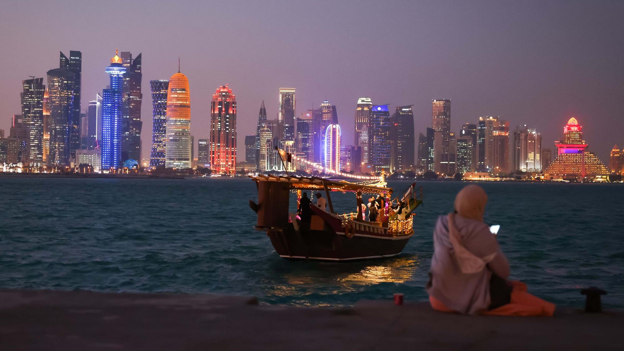 Eine Frau schaut auf ihr Smartphone vor der Skyline von West Bay Doha in Katar