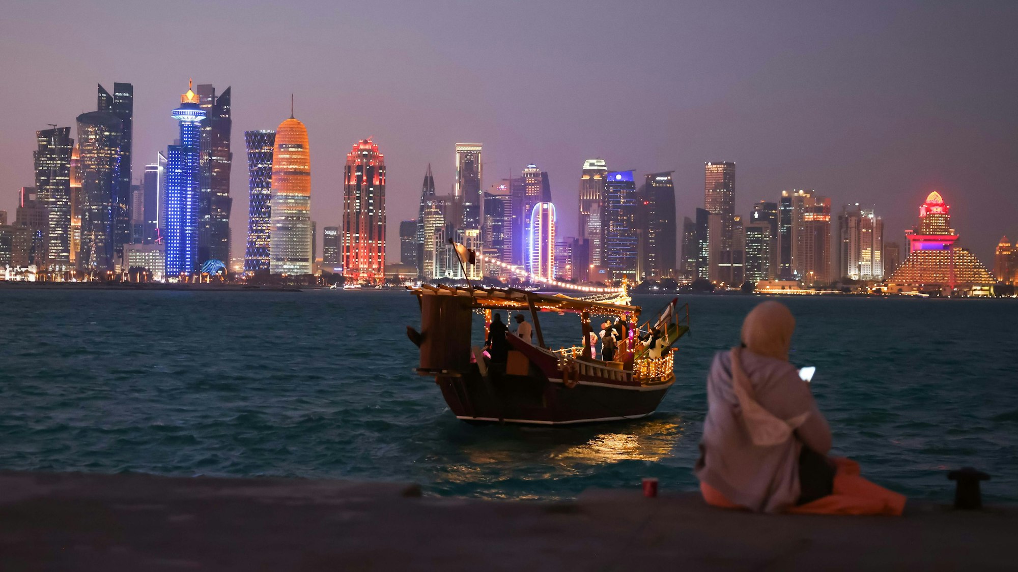 Eine Frau schaut auf ihr Smartphone vor der Skyline von West Bay Doha in Katar