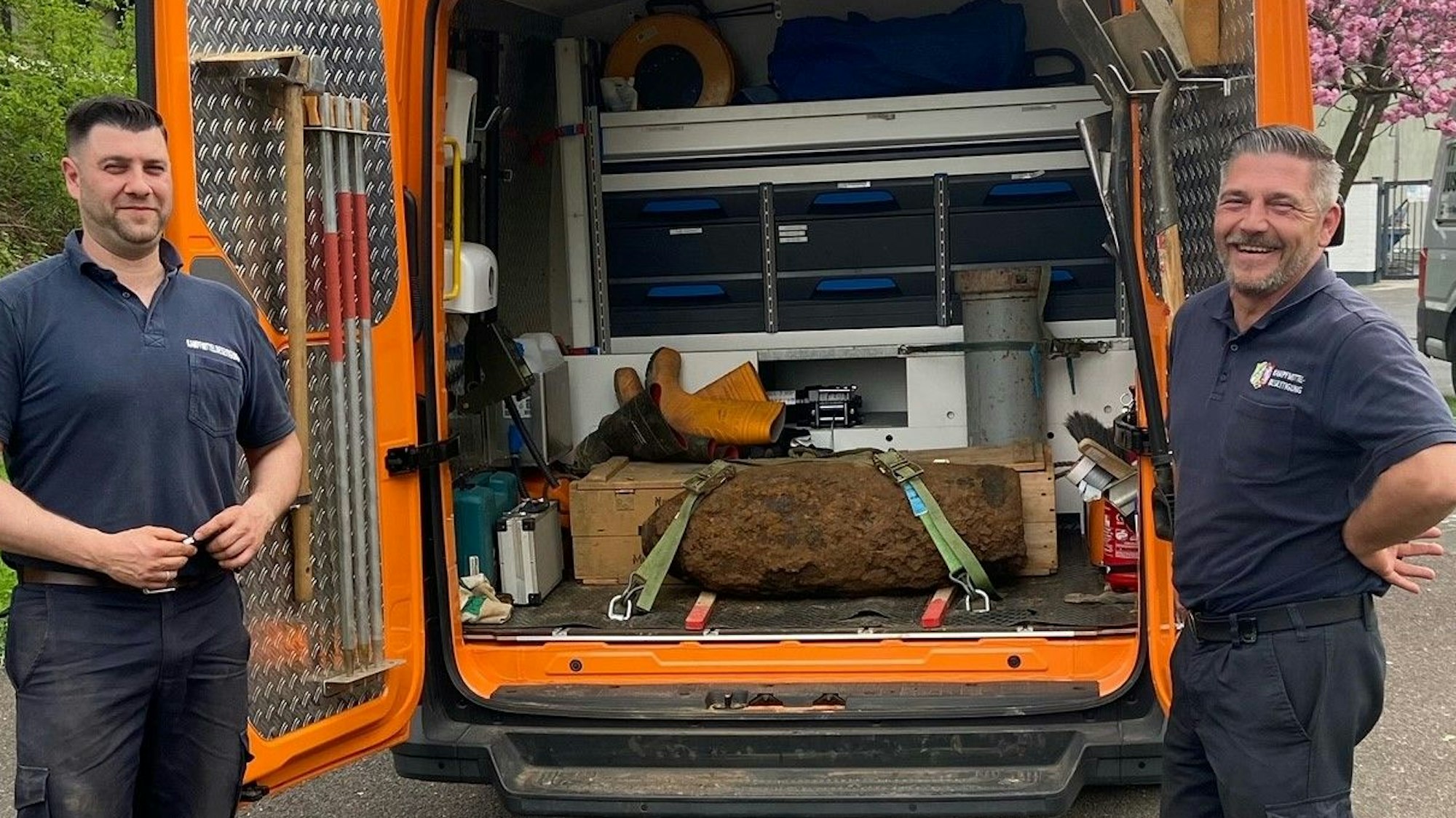 Zwei Männer stehen neben einem Fahrzeug, auf dessen Ladefläche eine entschärfte Bombe liegt.