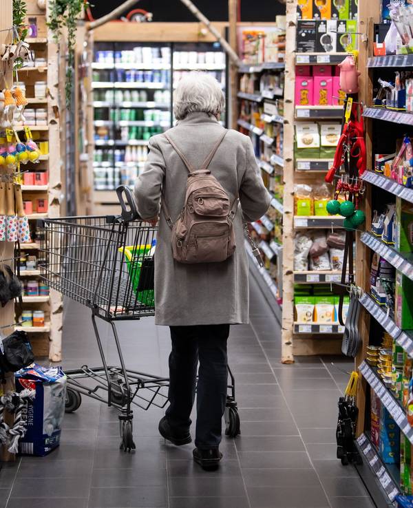Eine Frau geht mit ihrem Einkaufswagen durch einen Supermarkt.