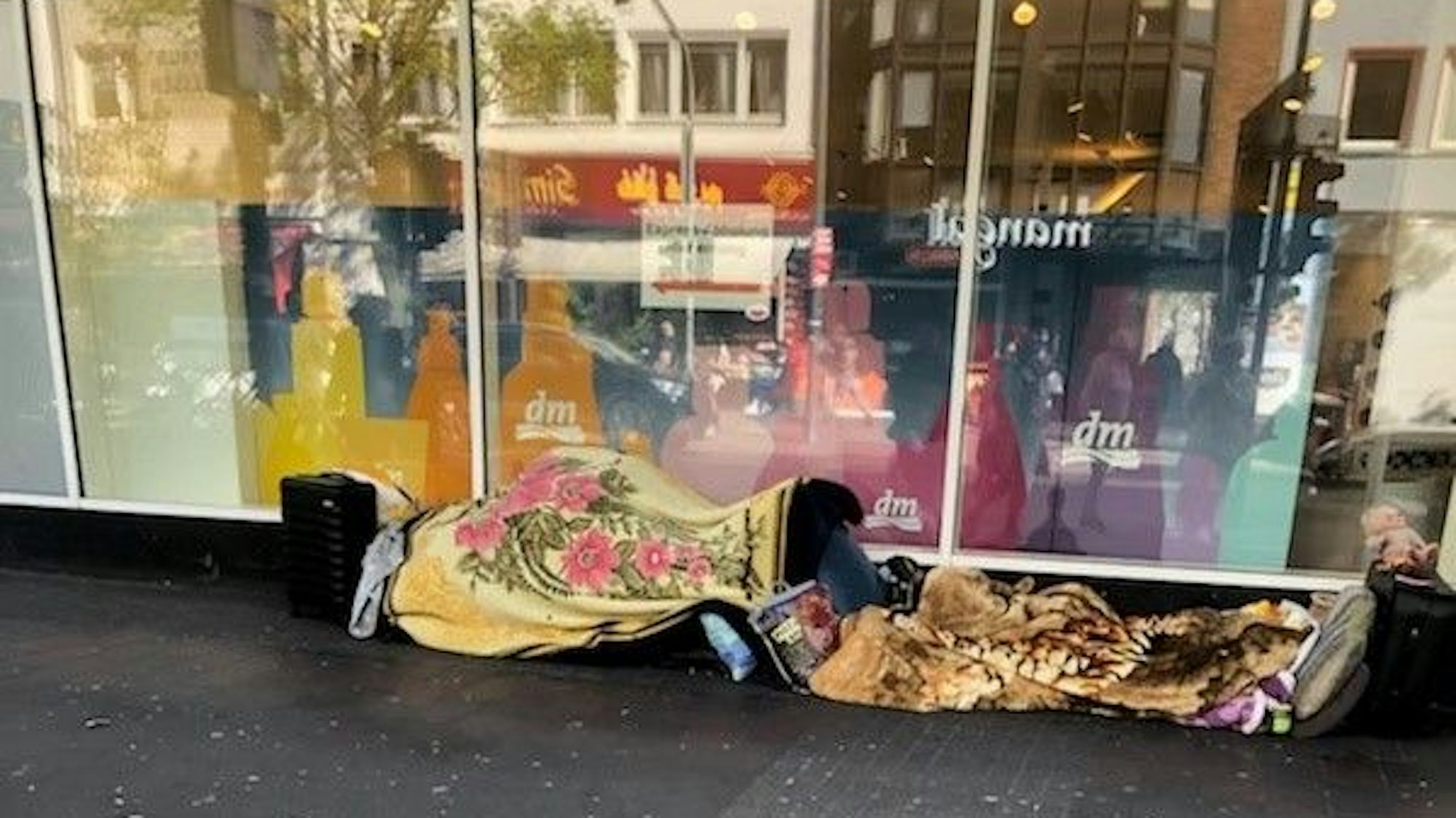 Decken, Kissen, Plüschtiere und Koffer befinden sich vor dem Schaufenster einer dm-Filiale in Köln-Kalk.