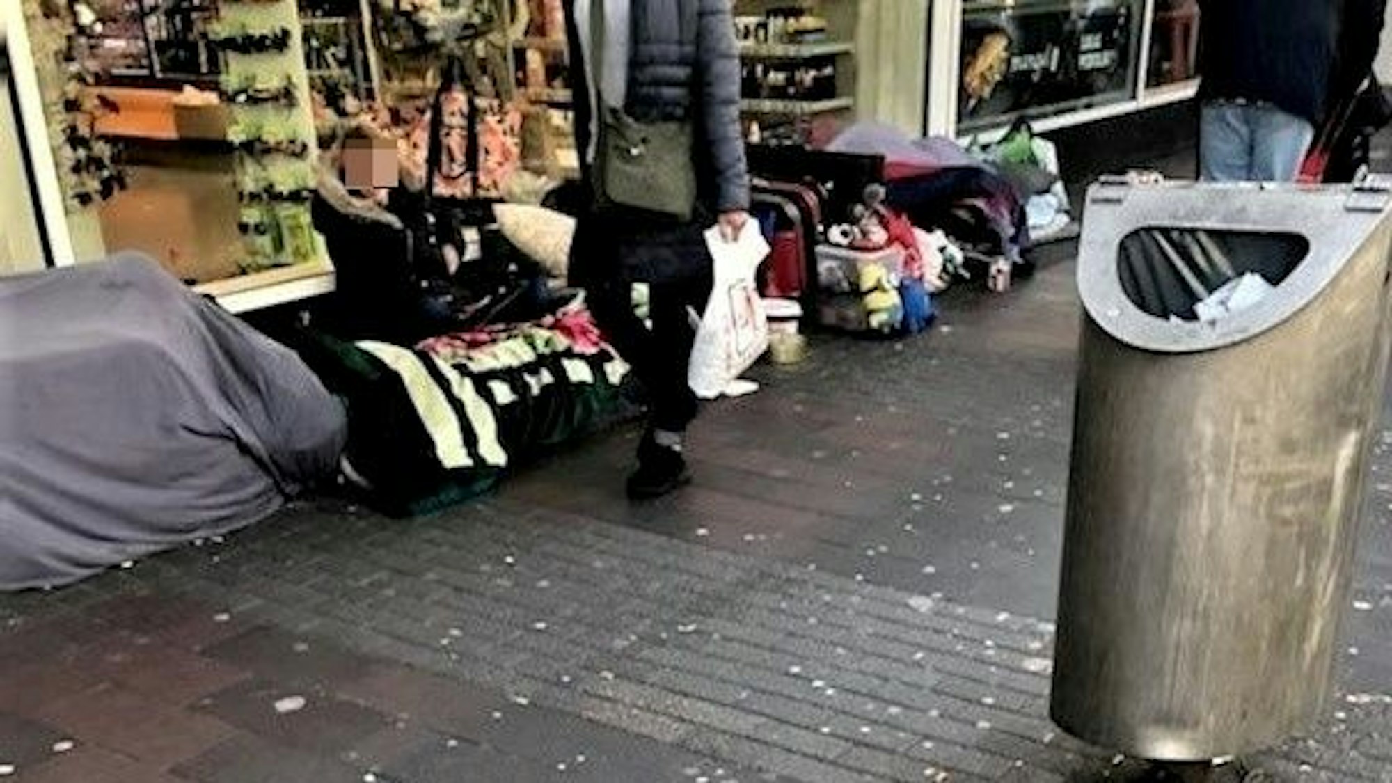 Provisorische Schlafstätten, Koffer und diverse andere Gegenstände befinden sich vor dem Schaufenster eines Geschäftes.