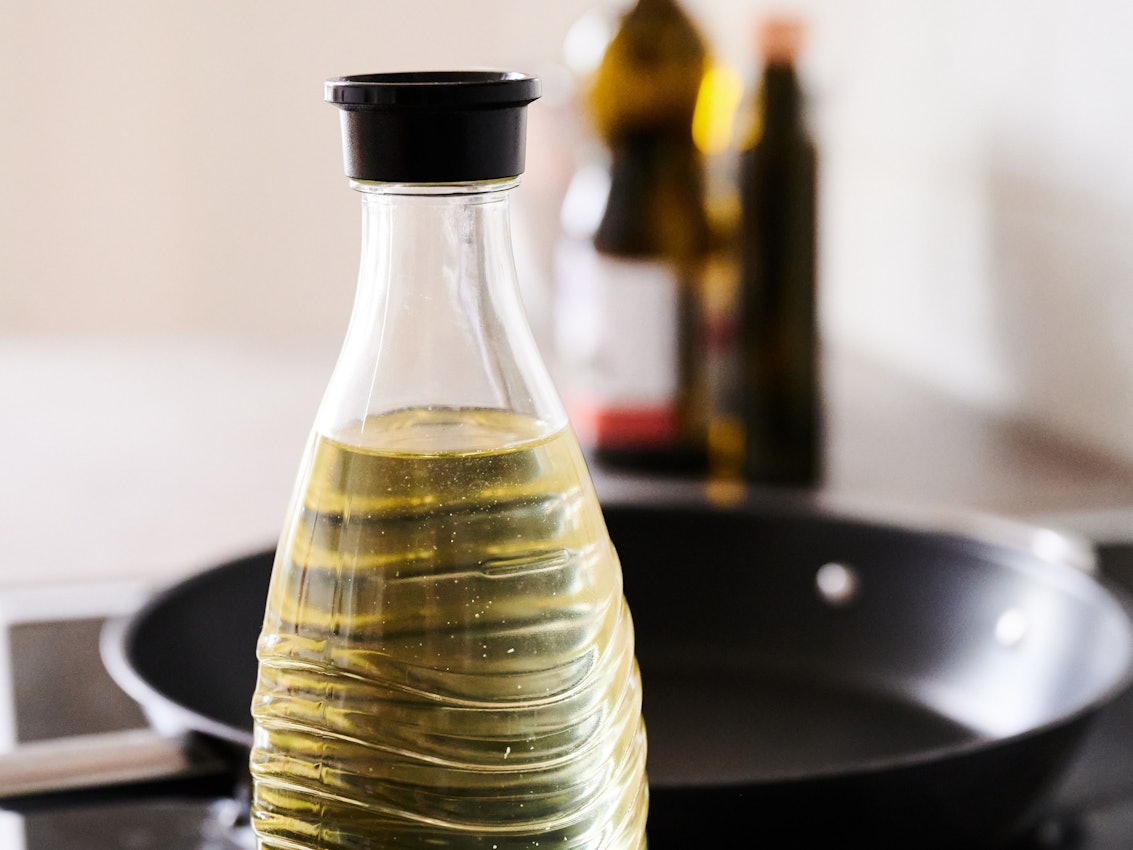 In eine Glasflasche abgefülltes Sonnenblumenöl steht neben einer Pfanne in einer Küche. Die Nachfrage nach Speiseöl und Mehl in Deutschland ist nach Beginn des Ukraine-Krieges zeitweise stark gestiegen.