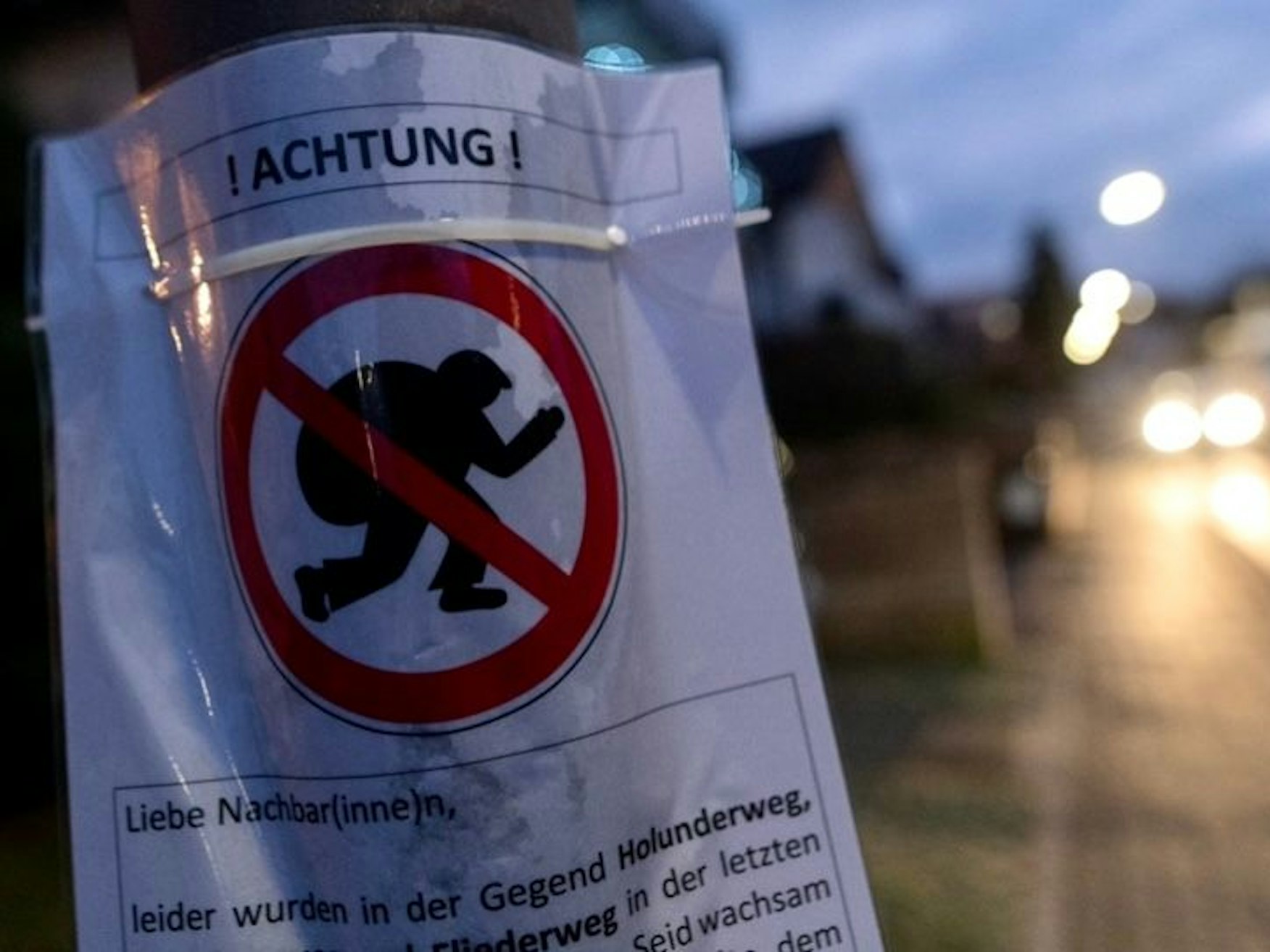 Ein Hinweisschild hängt an einer Laterne, auf dem vor Einbrechern gewarnt wird.