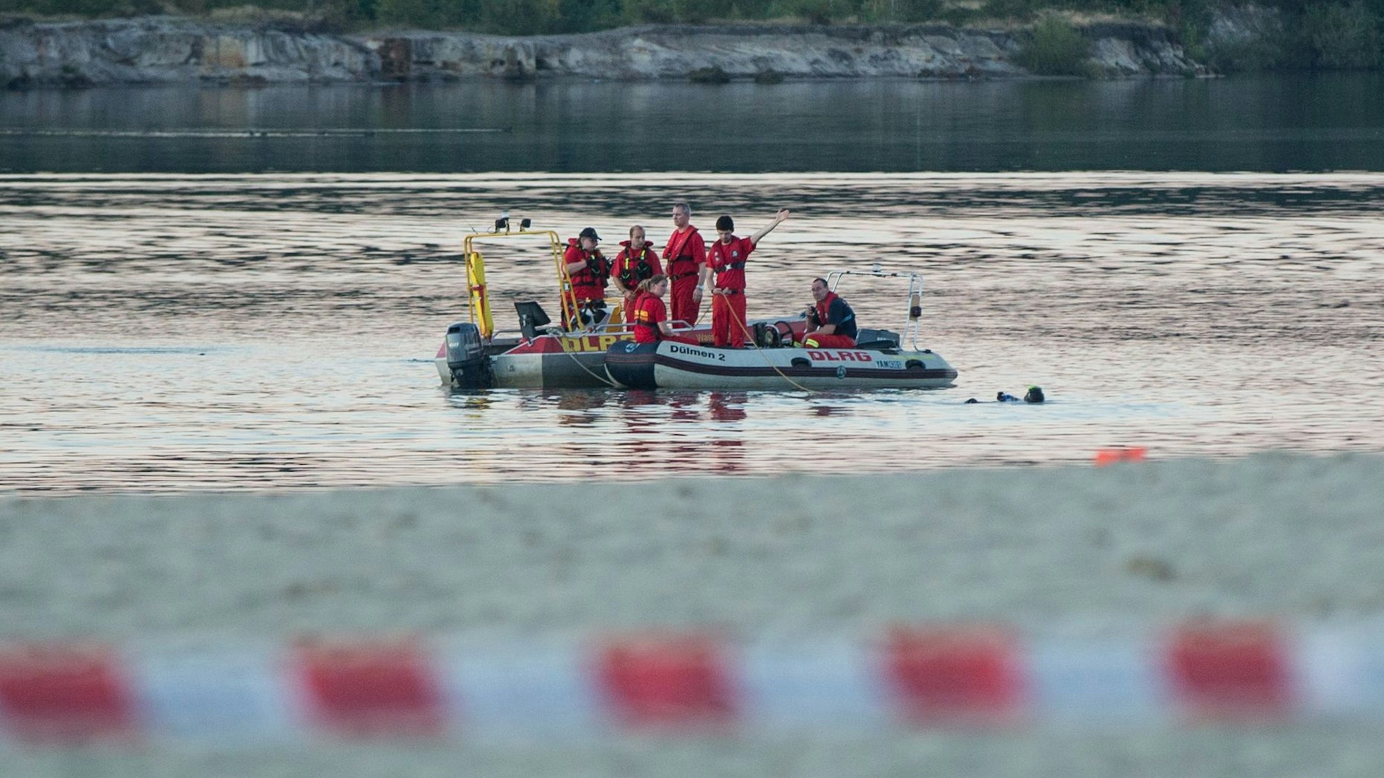 Einsatzkräfte der Feuerwehr und des DLRG fahren in Booten auf einem See.