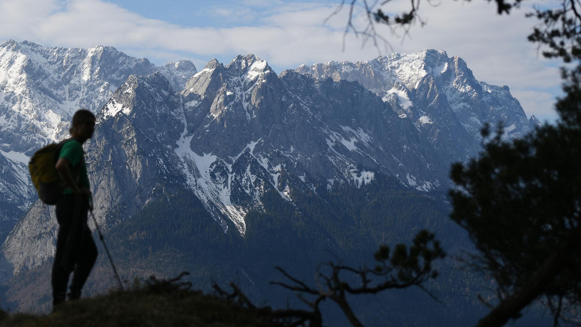Ein Wanderer steht vor den schneebedeckten Gipfeln des Wettersteingebirges, rechts ist die Zugspitze zu sehen.