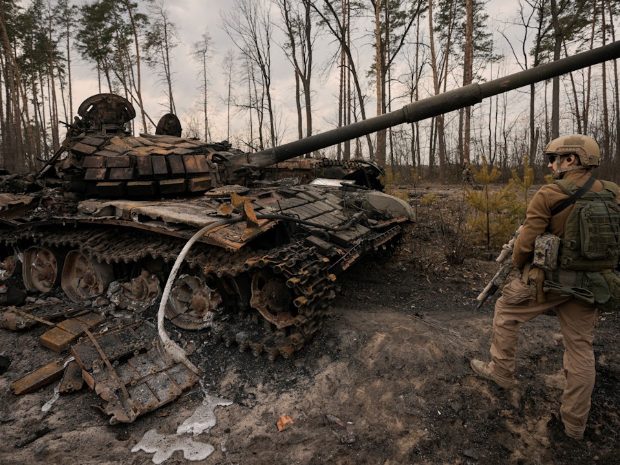 Ein ukrainischer Soldat steht am Stadtrand von Kyjiw neben einem zerstörten Panzer.