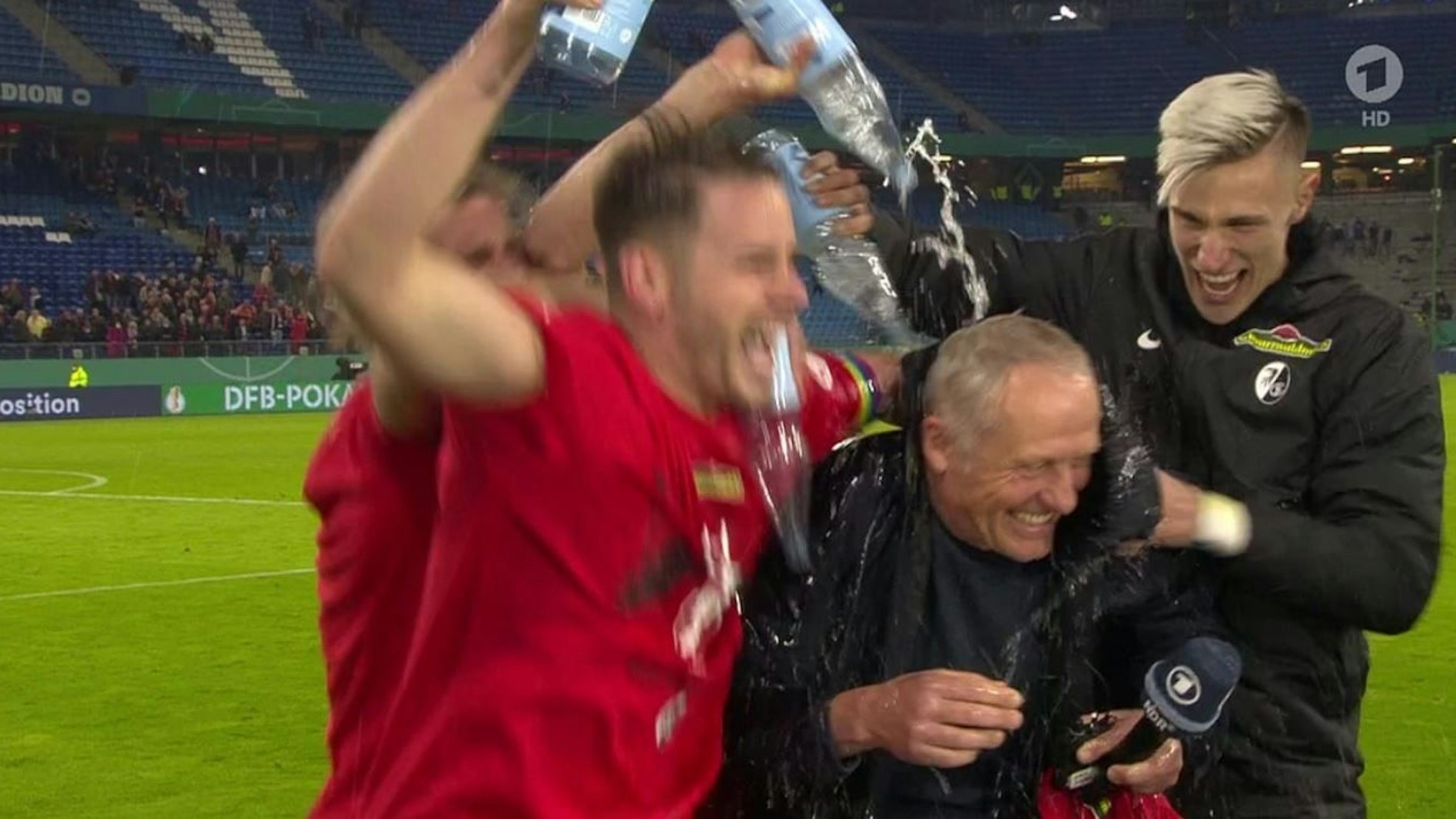 Beim Interview mit Jessy Wellmer von der ARD: Christian Streich wird von seinen Spielern geduscht.