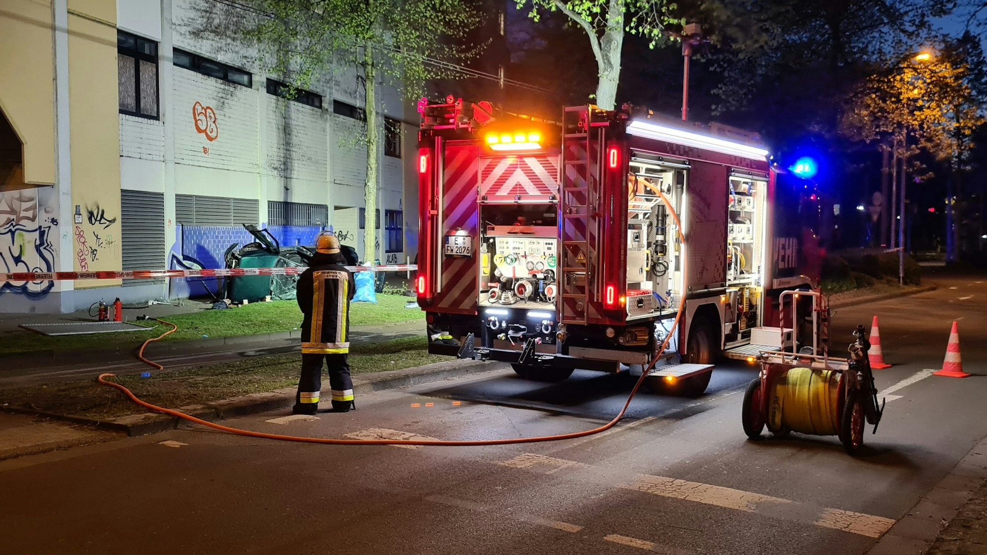 Ein Feuerwehrmann steht neben dem Wrack eines Autos. Zwei junge Männer sind am Ostersonntag in Essen mit einem Auto aus der obersten Etage eines Parkhauses gestürzt und ums Leben gekommen.
